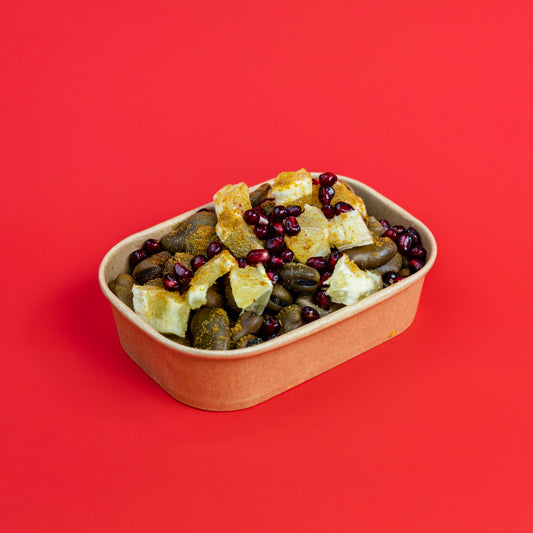 A small brown paper food container filled with mixed nuts, dried fruit pieces, and dark berries, photographed on a solid bright red background.