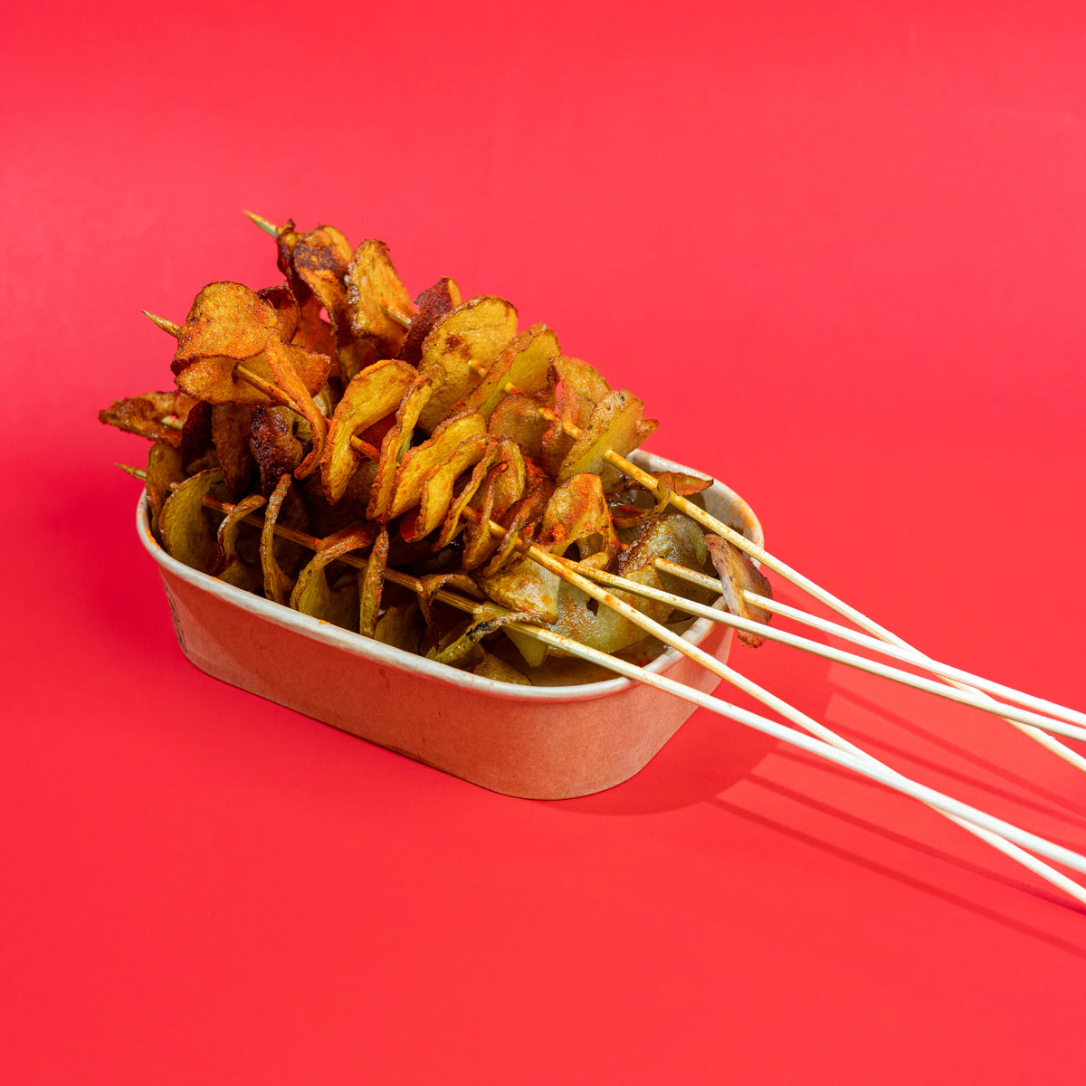 A metal tray filled with skewered roasted food, photographed on a solid bright red background.