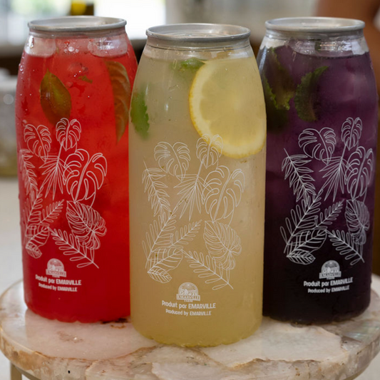 Three beverage cans displayed on a round marble-and-gold pedestal stand on a countertop, with a blurred indoor background and part of a person visible at the right edge.